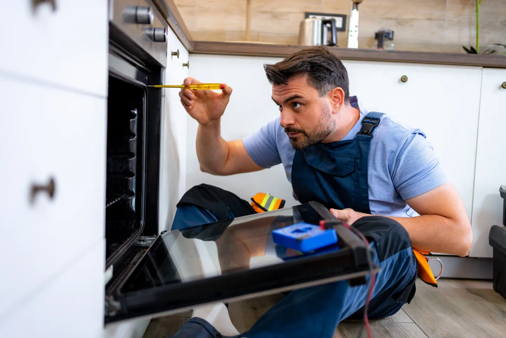 Oven repair technician using screwdriver to fix broken heating element.