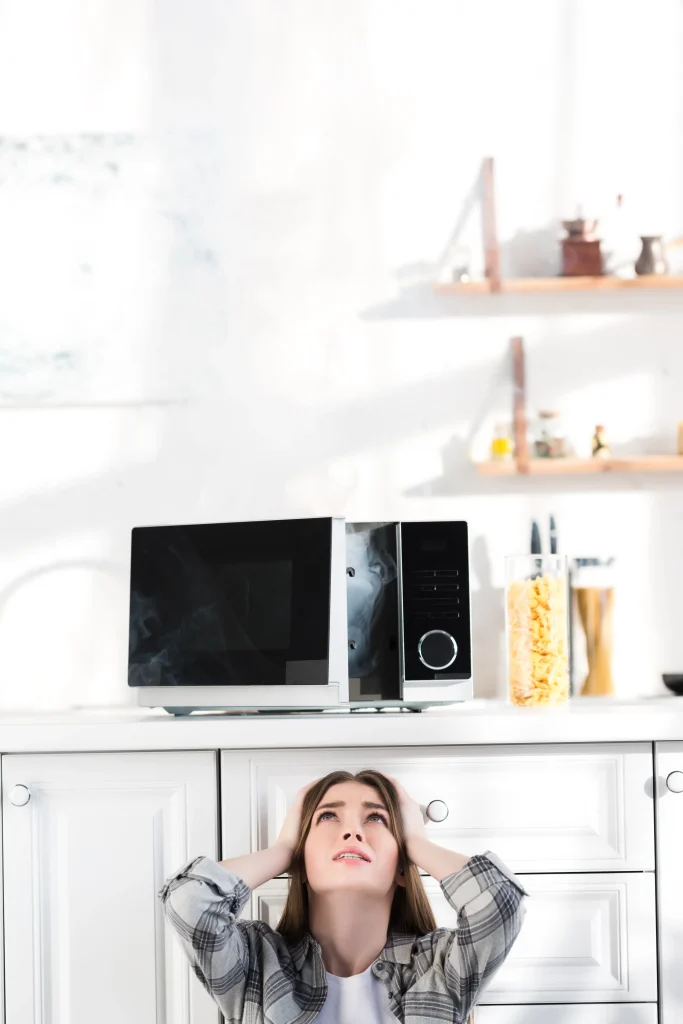 Woman looking frustrated at broken microwave in modern kitchen